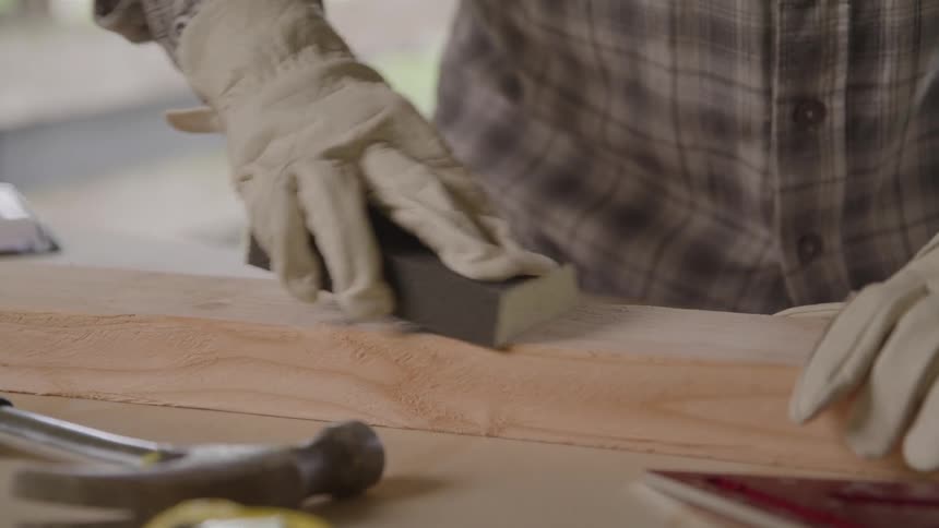 A person sands a piece of wood in a workshop