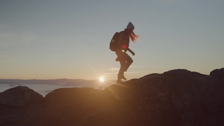 Woman hikes over uneven rocky terrain while the sun shines from the horizon