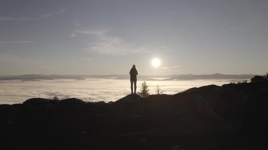 Person standing on a rock watching the sunrise above a sea of clouds
