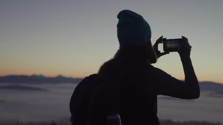 Person with backpack and beanie captures the sunrise with a phone