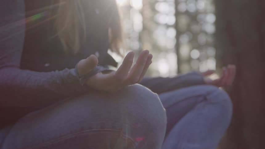 Woman meditates while sitting in the woods on a sunny autumn day