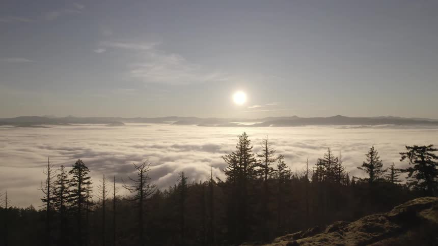 Woman standing on rocks watching the sunrise above a sea of clouds