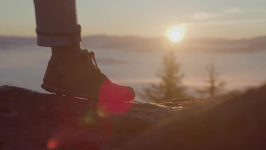 Person walking on a rock in the mountains with the sun on the horizon