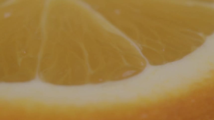 A macro shot shows the vibrant translucent segments of a sliced orange which are full of juice sacs the shot is static and filled with the bright orange and yellow colors of the fruit
