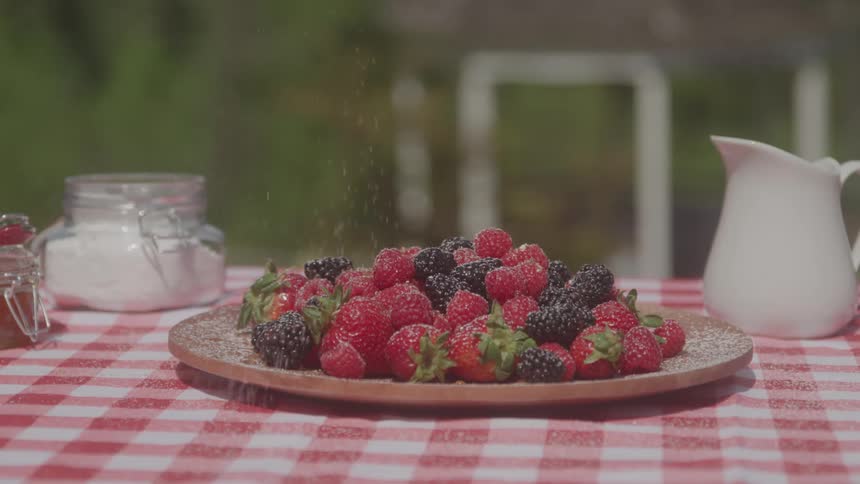 Strawberries and blackberries on a table with powder being sprinkled on them on a sunny day