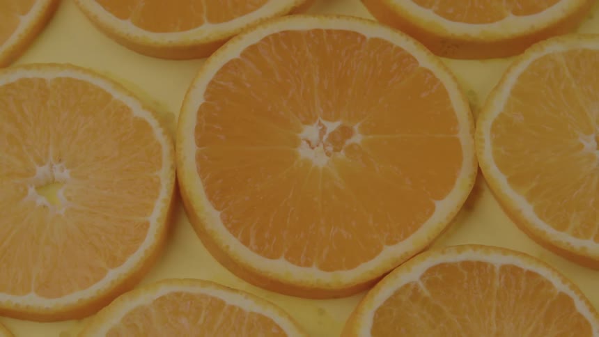 A topdown view shows multiple bright orange slices arranged on a light yellow background the slices are all round and their white rinds and juicy segments are clearly visible