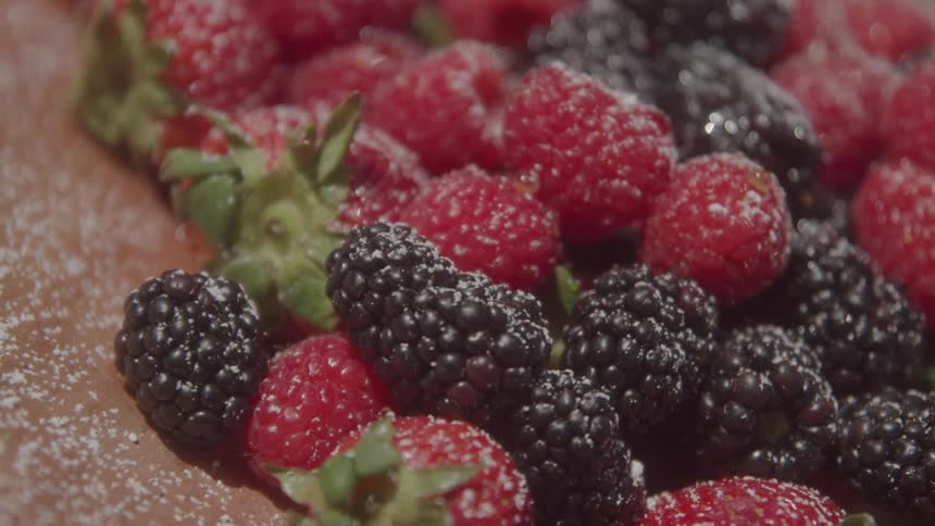 A variety of berries including raspberries and blackberries some lightly dusted with a white substance likely powdered sugar or frost on the surface