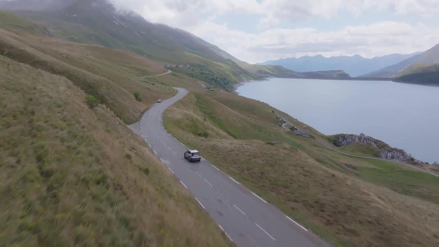 Car driving along a winding road by a lake surrounded by mountains
