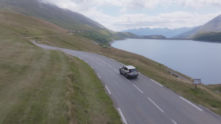 Car drives along a winding lakeside road in a mountainous region
