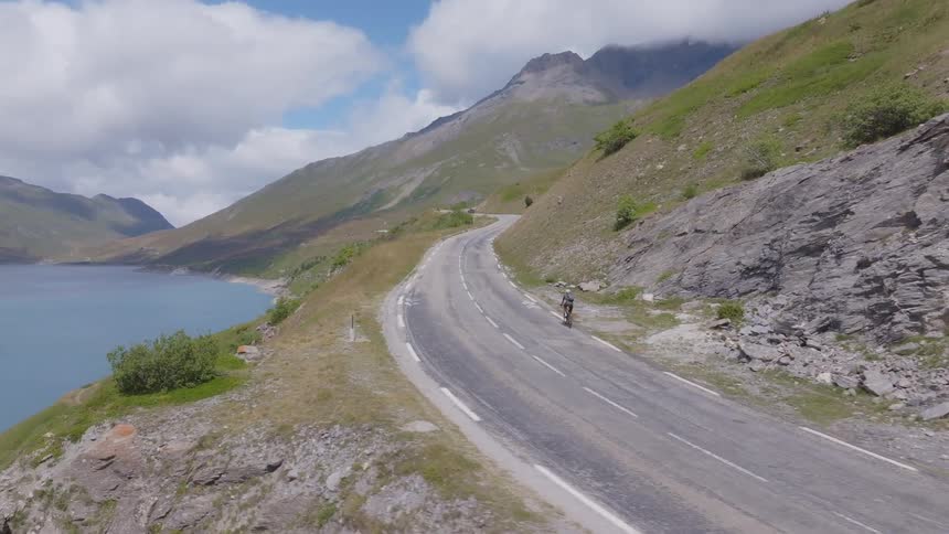 Cyclist riding on a winding road by a lake in the mountains