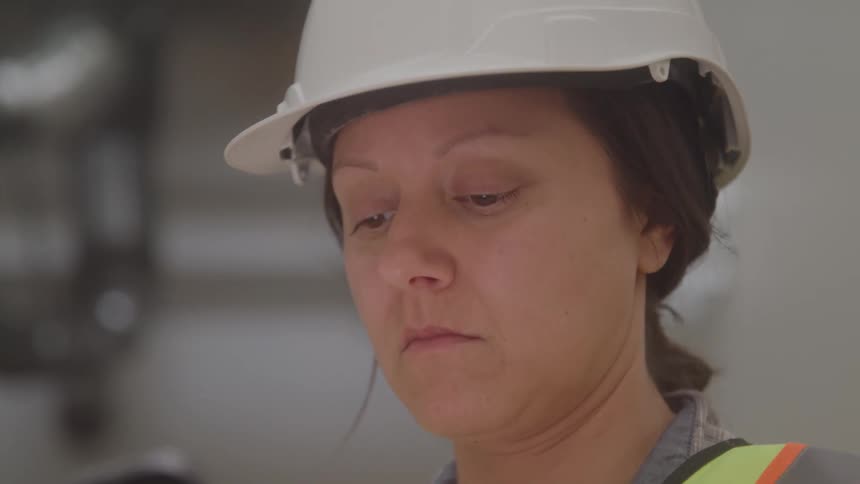 Woman wearing a safety helmet and reflective vest carefully observing an object
