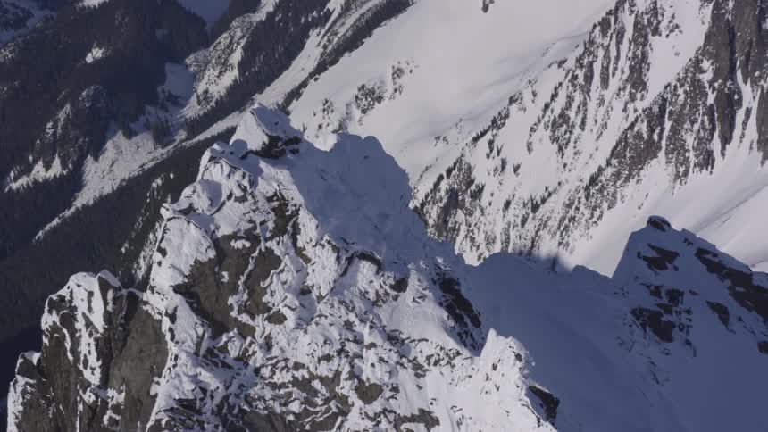 Snowcovered rocky peak with steep slopes surrounded by snowy mountains