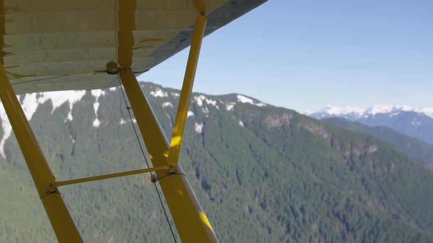 An airplane flies over a mountain range covered in green vegetation at midday
