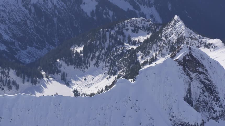 A snowy mountain ridge rises through pinecovered slopes