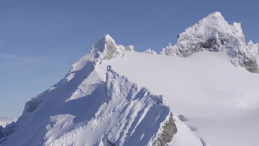 Snowcovered jagged mountain peaks rise sharply against a clear blue sky