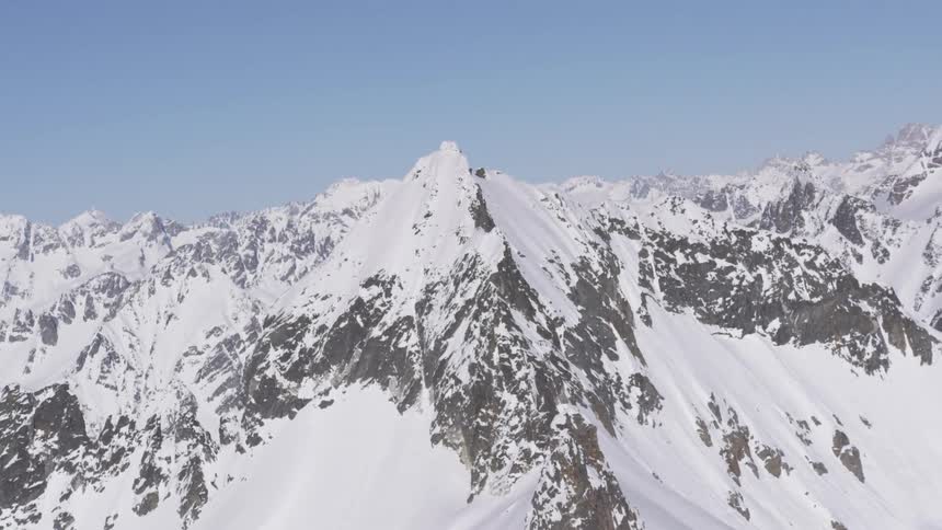 A massive snowcovered mountain range with sharp rocky peaks under a clear pale blue sky