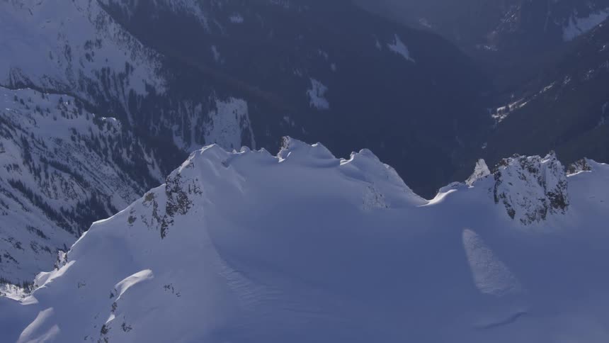 Sunlit snowy ridges with a dark valley in the background