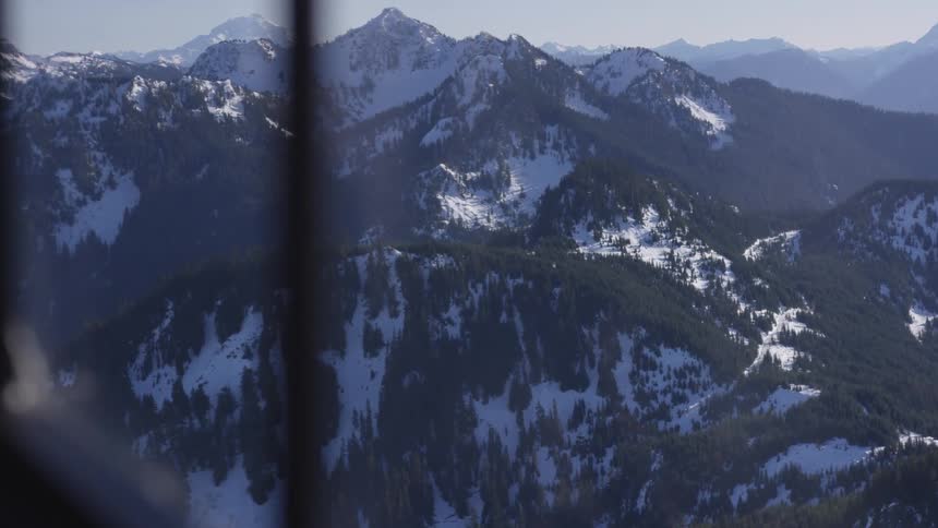 An aerial view of a snowcapped mountain range dotted with pine tree forests