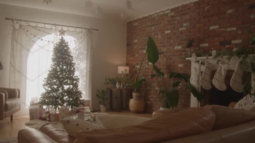 Living room decorated for christmas with a lit tree stockings on the fireplace and gifts around