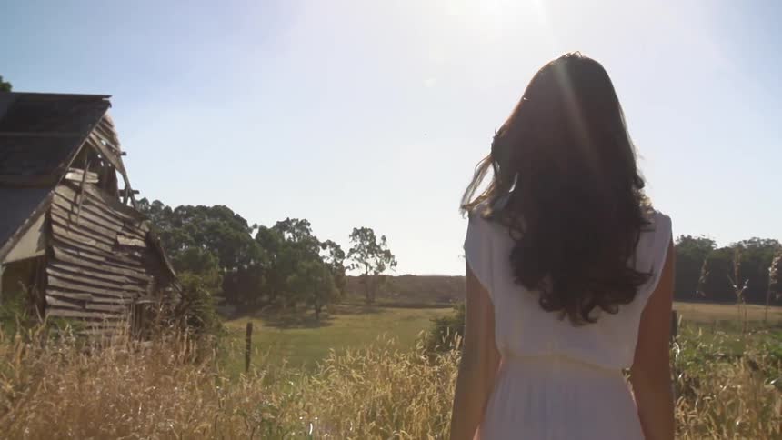 Woman walking by a dilapidated building in a grassy field