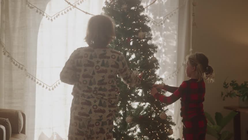 Brother and sister decorating christmas tree in thier pajamas in the morning