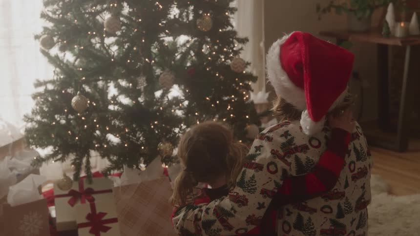 Children hugging watch a decorated christmas tree surrounded by gifts