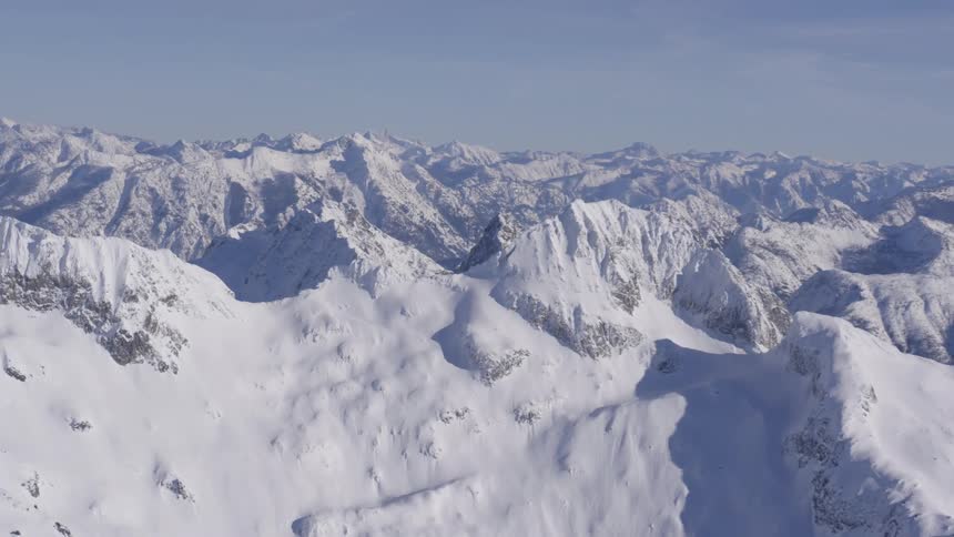 A mountain range with a wide landmass featuring a series of mountains all covered in snow on a sunny winter day