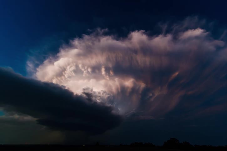 A massive storm with lightning glows in the warm sunset light