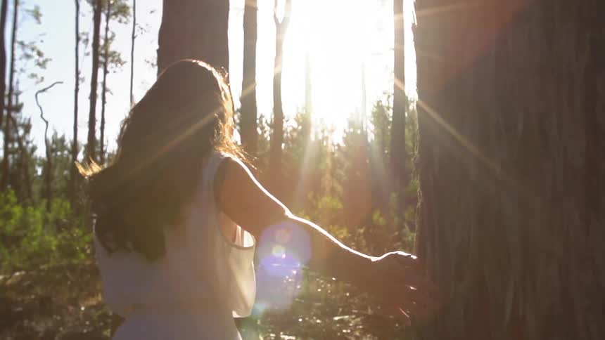 Woman walking through some woods with the sun high
