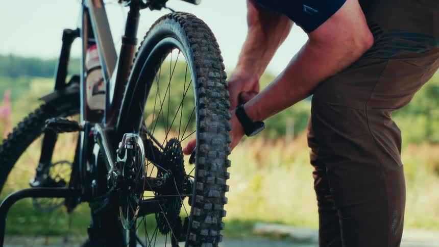 A man uses a tool to adjust the rear wheel components of a mountain bike on a sunny day