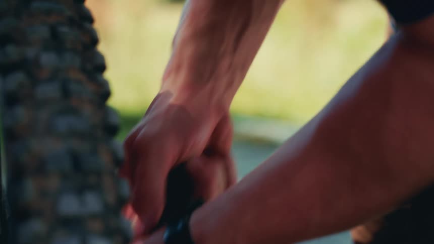 The video shows a closeup of a persons hands and arms the person is using a bike pump to inflate a tire the background is out of focus and the video has a watermark that says filmsupply
