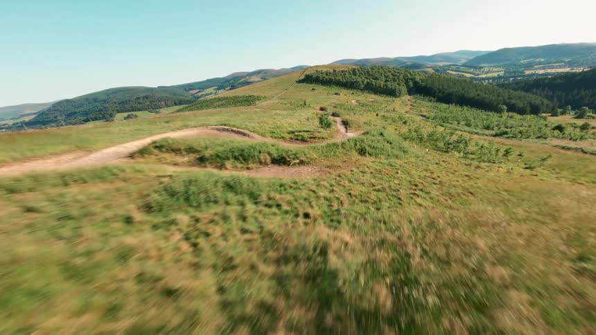 Cyclist rides at high speed along a dirt trail surrounded by hills