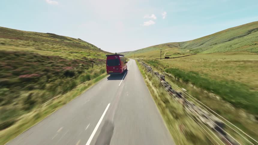 A red delivery van drives on a rural road through green hills