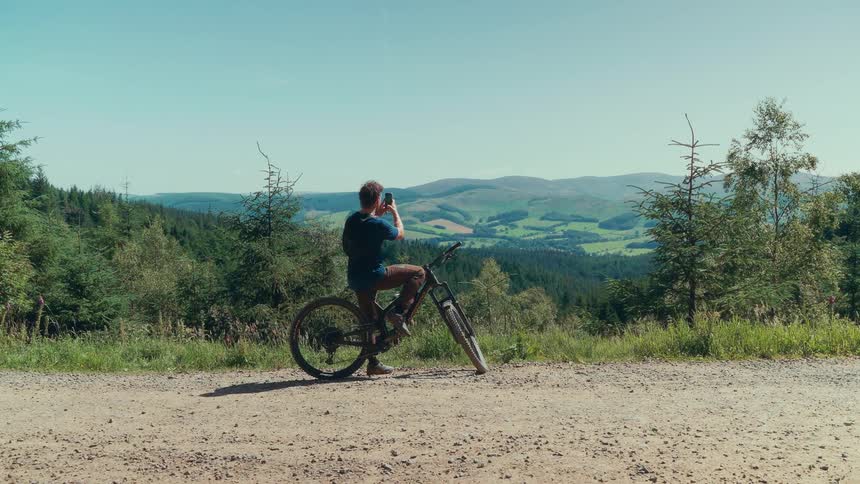 A man stops on his bike to photograph a mountain landscape