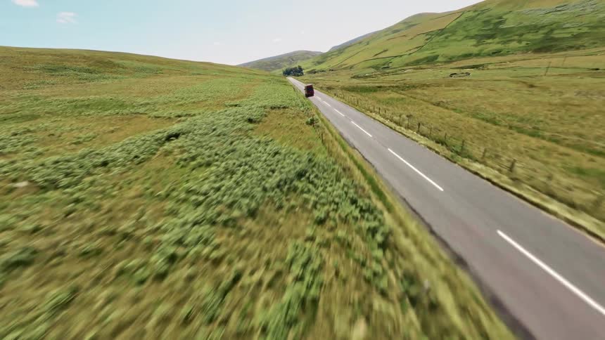 A red van drives on a freeway in a rural area surrounded by open grasslands at midday