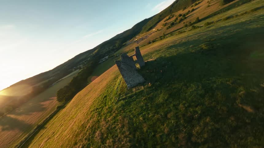 Stone ruins stand isolated on a green hillside at sunset