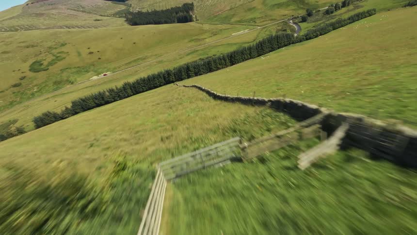 A river winds through open green fields and hills under a clear sky