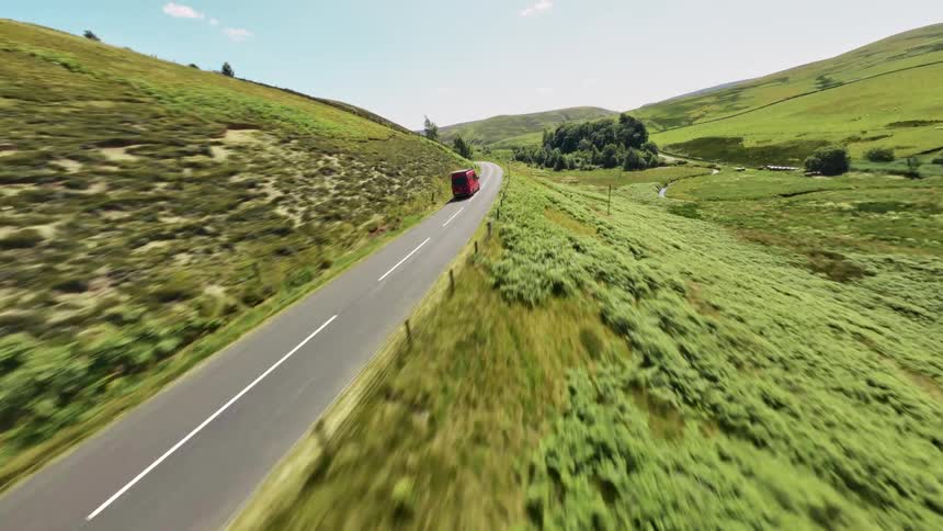 Red van driving on a road between green hills