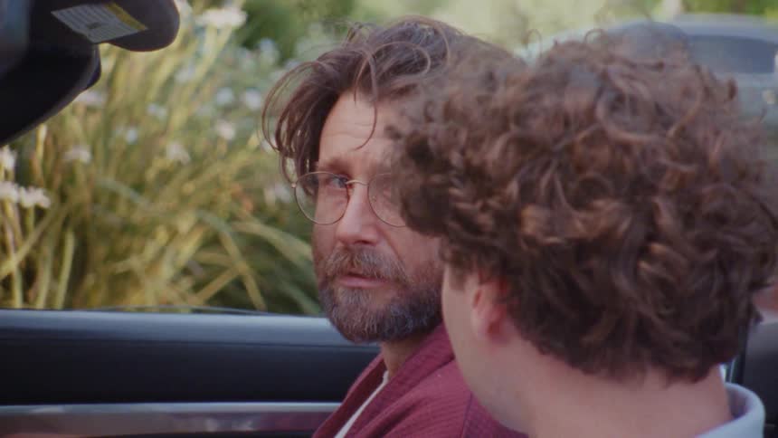 Two men sit in an openroof car having a discussion at midday