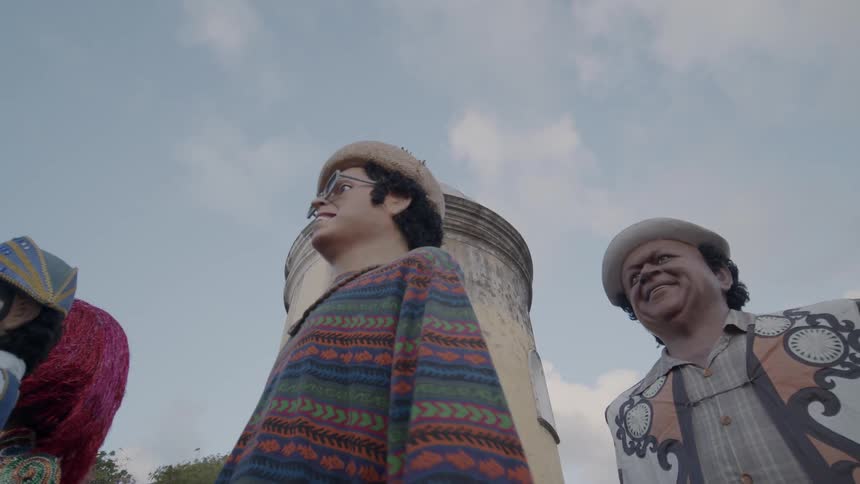 Giant puppets dressed in colorful costumes stand in front of a yellow tower