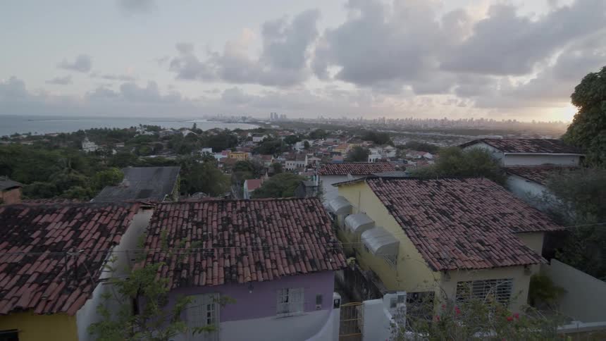 Red roofed homes stand in a residential neighborhood on the outskirts of a coastal city near sunrise