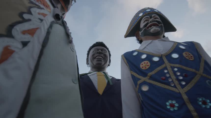 The video shows a lowangle shot of a group of people with a focus on several large costumed statues or effigies the statues are dressed in colorful and ornate outfits and they appear to be part of a parade or a cultural festival the background is a