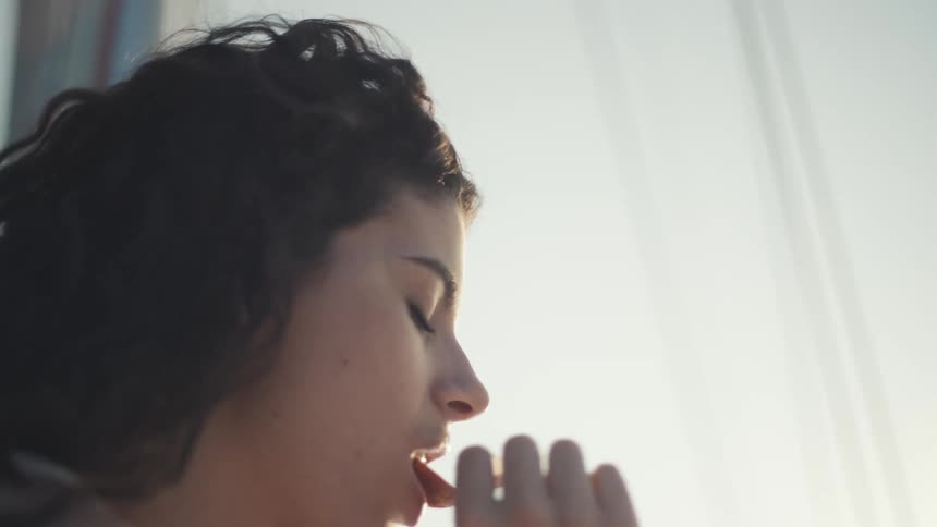 A young woman with dark curly hair puts a piece of food in her mouth