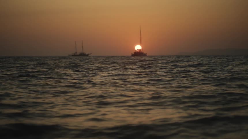 A beautiful sunset over a vast ocean with two sailboats silhouetted on the horizon