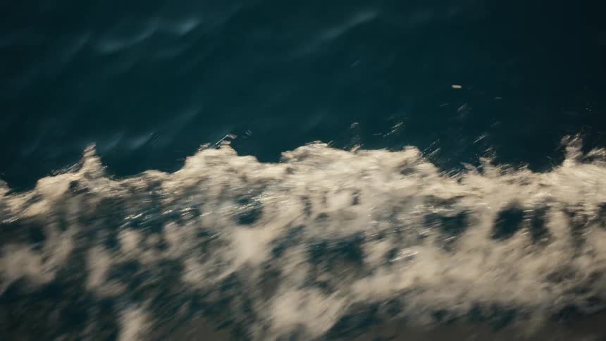 Surging water foams slightly against the flowing blue ocean water during the daytime