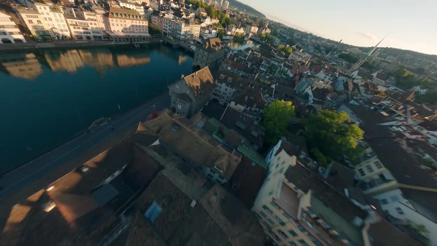An aerial drone shot captures the city of zurich from above featuring the limmat river historic buildings and distant hills all bathed in the warm light of sunrise
