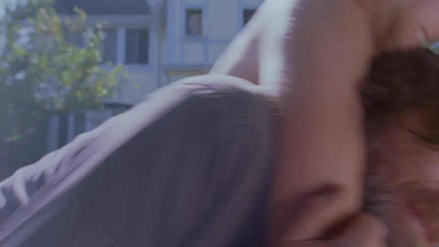 The face of a bearded man who is being held down by a boy wearing a white tank top