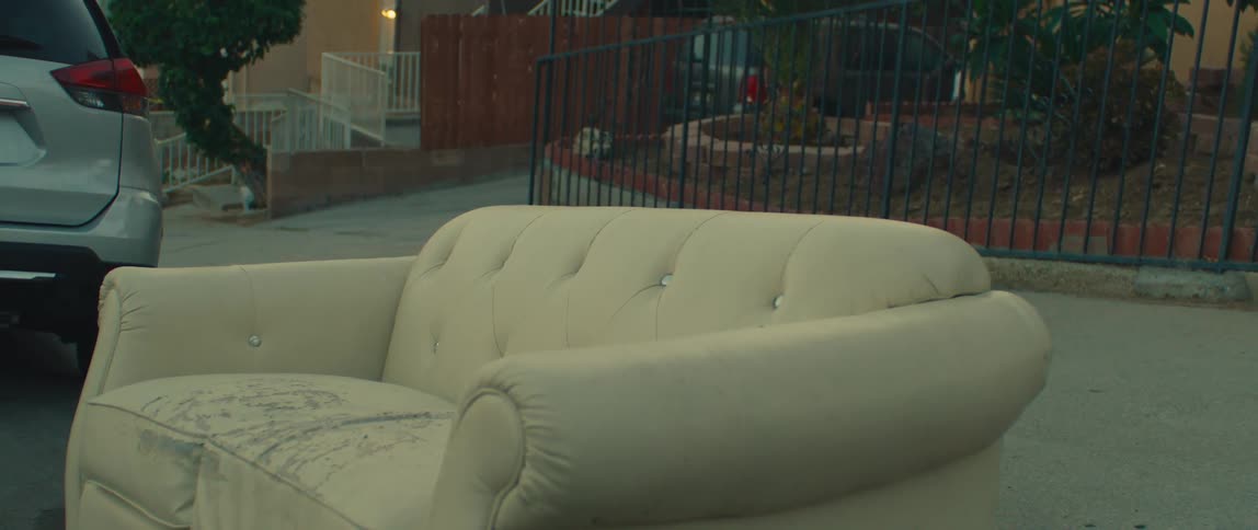 A dirty discarded couch and other furniture items on a residential street
