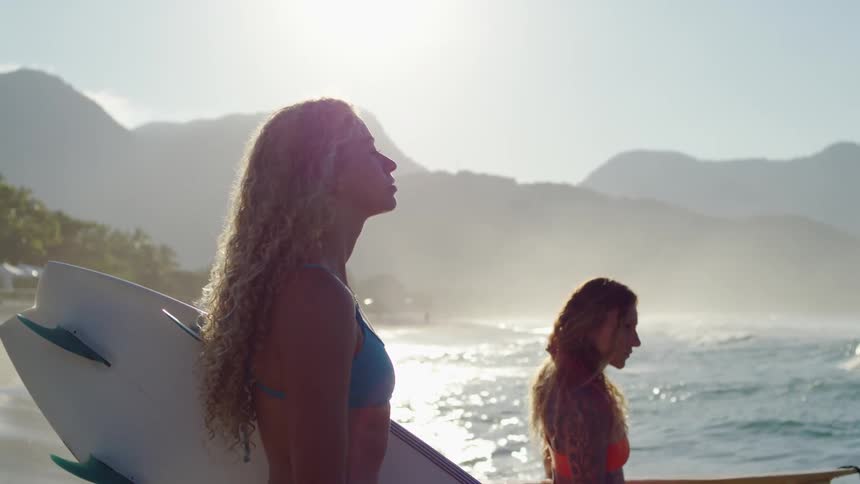 Two female surfers standing at shoreline watching waves