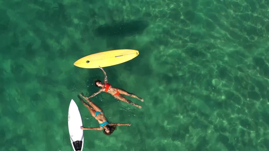 Two women in bikinis floating in the sea with surfboards nearby